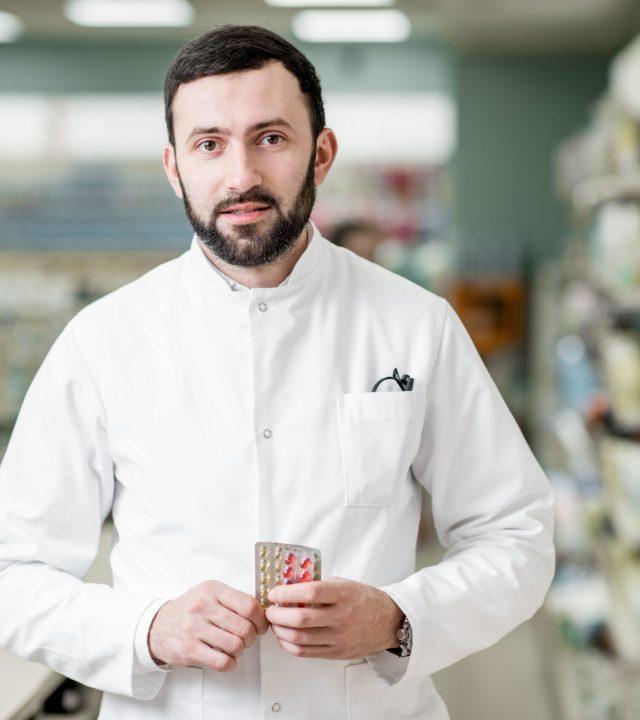 Portrait of man pharmacist standing at the paydesk selling medications in the pharmacy store