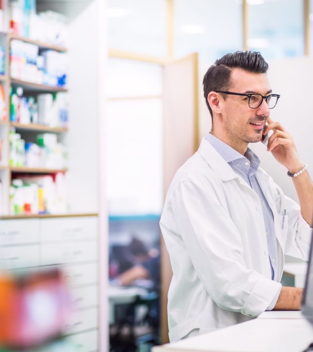 Portrait of a young atrractive friendly male pharmacist with a smartphone. Man making a phone call.